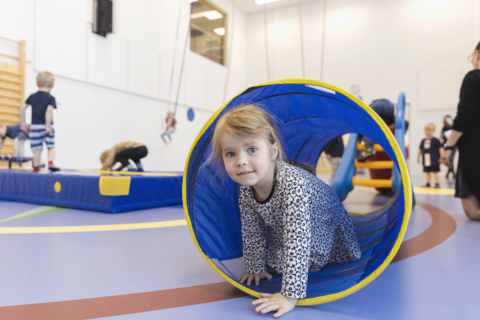 Lapsi kurkistaa jumppasalin tunnelista.