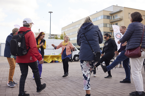  A group of people are excercising in a circle in a market square.