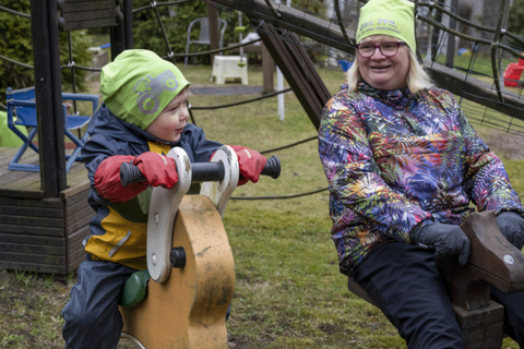 Lapsi ja hoitaja keinuvat leikkipuistossa. 