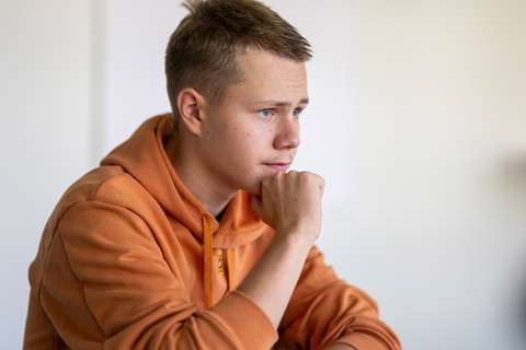 Roope Kuossari istumassa oikea käsi leuan alla, oranssi huppari päällä