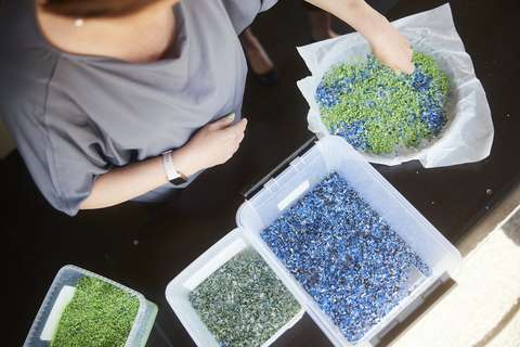 Blue and green crushed plastic is sprinkled from boxes onto a baking paper.