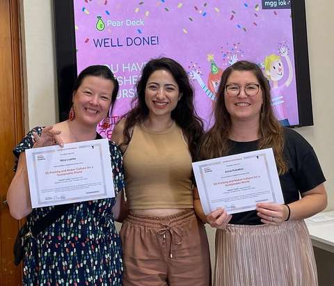 Kaksi opettajaa diplomit käsissään hymyilevät yhdessä kouluttajan kanssa.