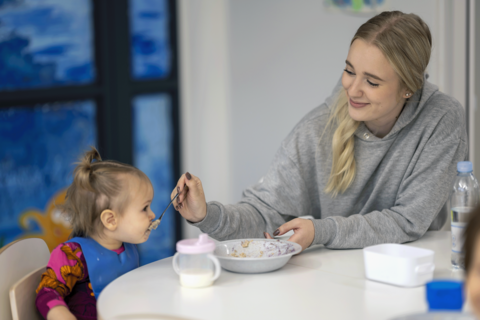 Hoitaja auttaa lasta ruokailemaan.