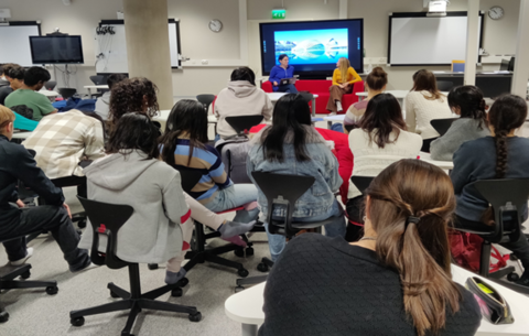 A group of students watching a teacher to interview a student about her essay.