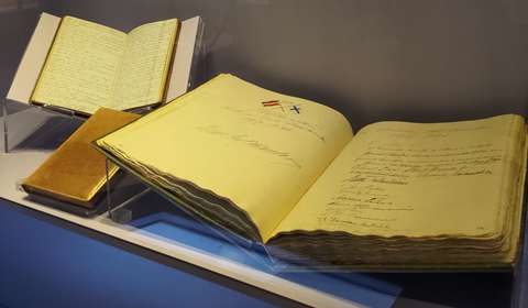 Yli sata vuotta vanha vierakirja, johon on käsialalla kirjoitettu tapahtumia ja vieraiden nimiä.