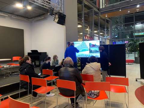 Ihmisiä kerääntyneenä tarkastelemaan esitystä tv-ruudulta.