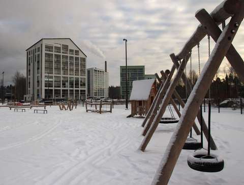 Kuva talvisesta Syvänsalmenpuistosta. Etualalla keinuja, joiden takana on muita leikkivälineitä. Kuvan taustalla näkyy asuinkerrostaloja.
