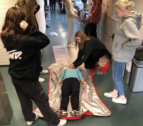 yksi opiskelija esittää pyörtynyttä maaten lattialla ja muut opiskelijat auttavat häntä