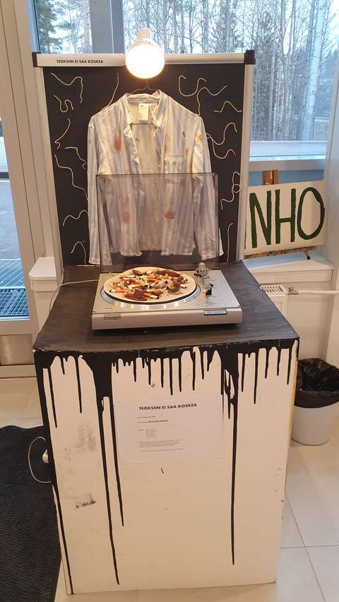 taideteos jossa paita ja levysoitin. levysoittimella tupakantumppeja sekä tehtyjä etanoita