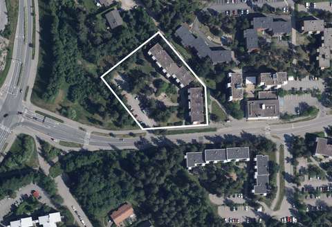 Ilmakuva, jossa näkyy kerrostaloja sekä pientaloja metsäisen puuston lomassa. Suunnittelualueen kaksi kerrostaloa sekä pysäköintialue on rajattu valkoisella viivalla.