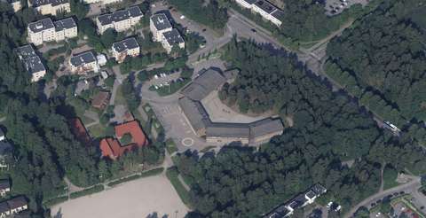 There are trees and blocks of flats in the vicinity of the large school building.