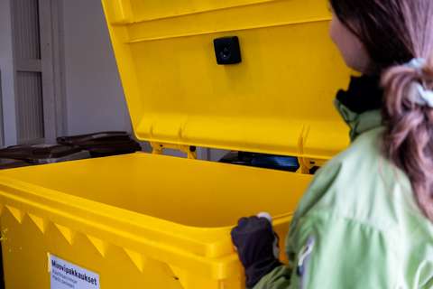 A black device on the inside of the lid of a yellow plastic recycling bin as a person holds the lid open.