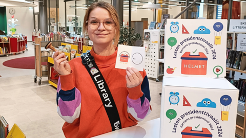Kirjastoneuvoja Jenna Nokkala vaaliuurnan äärellä valmiina toimimaan vaalivirkailijana lasten omissa presidentinvaaleissa.