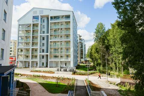 Flervåningshus, träd med gröna blad, en fotgängare som går på en gångväg.