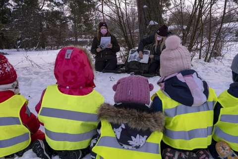 Lapset istuvat maassa ja katsovat, kun ohjaajat piirtävät tarinaa.