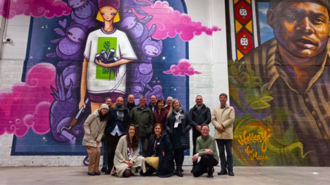 A group of people in winter clothes poses for a photograph inside Keran Hallit in front of murals.
