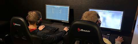 Kaksi henkilöä tuoleilla tietokoneiden äärellä.