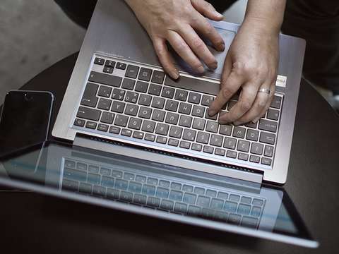 Writing hands are shown on the keyboard of the laptop.