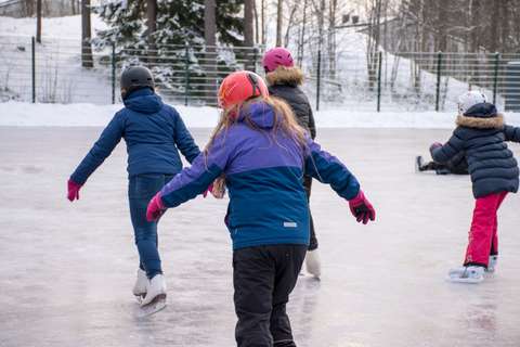 Kuvassa neljä lasta luistelee ulkojäällä pois päin kamerasta.