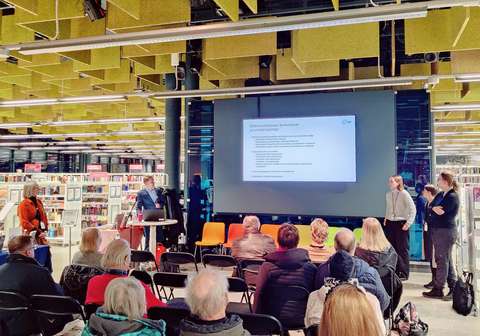 Entressen Estradilla yleisöä ja esiintyjiä katsomassa infotaululla näkyviä dioja.