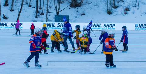 Kuvassa ryhmä lapsia pelaa jääkiekkoa ulkojäällä jääkiekkovarusteissa.