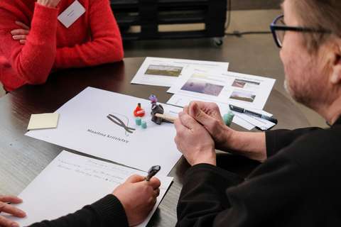 Three people sitting at a table. There are papers and crafting materials on the table.