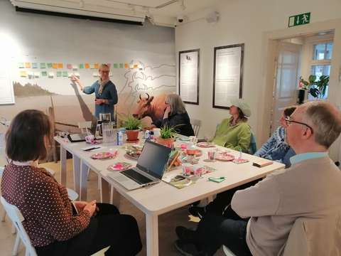 KAMU's volunteers "kampparit" are sitting around a table and brainstorming. One stands in front of a wall with post it notes.