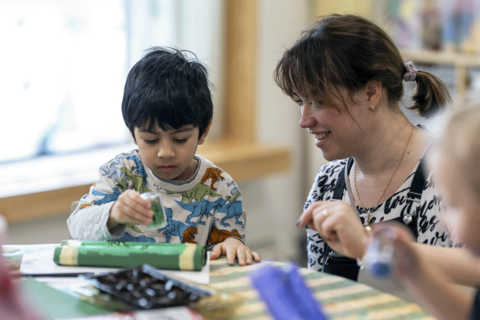 Opettaja auttaa lasta askartelussa.