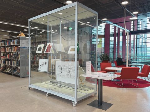 Suuri lasivitriini, jonka vieressä on pieni pöytä. Vitriinissä on esillä erikokoisia taideteoksia.