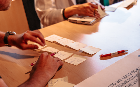 Henkilö kirjoittaa pöydällä oleville lapuille muistiinpanoja.