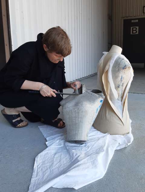 Konservaattori istuu lattialla ja rakentaa vaatetukea puusta.