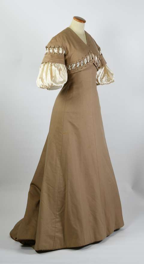 Vaaetuella ruskea pitkä mekko, jossa lyhyet pöyhkeät hihat.