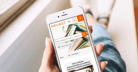 Käsi pitelee kännykkää, jonka näytöllä näkyy Helmet-verkkokirjasto.