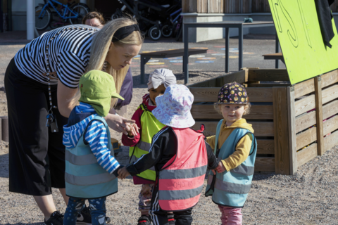 The teacher is chatting with the children in the daycare center's yard.