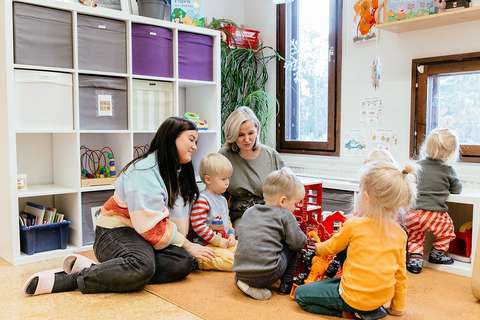 Karppinen ja Fredriksson istuvat lattialla yhdessä leikkivien lasten kanssa.