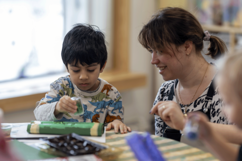 Opettaja auttaa lasta askartelussa.