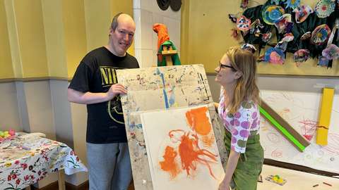 Kaksi henkilöä pitää maalaustelinettä.