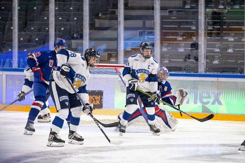Kuvassa on valko-sinisiin kisa-asuihin pukeutuneita jääkiekkoilijoita palaamassa jäähallissa.