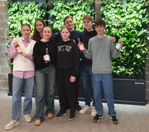 Seitsemän opiskelijaa seisoo viherseinän edessä. Kolmella on limupullot kädessä.