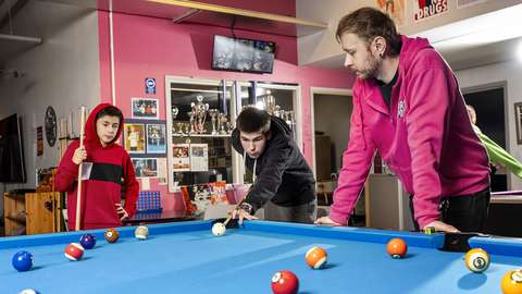 Young people play pool, the youth counselor follows next to them.