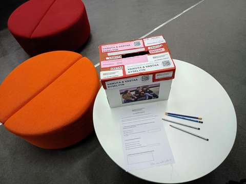 Kyselylomake, kyniä ja vastauslaatikko pienellä pyöreällä pöydällä.