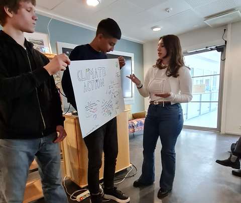 kolme opiskelijaa seisoo ja näyttää ryhmätyöpaperia