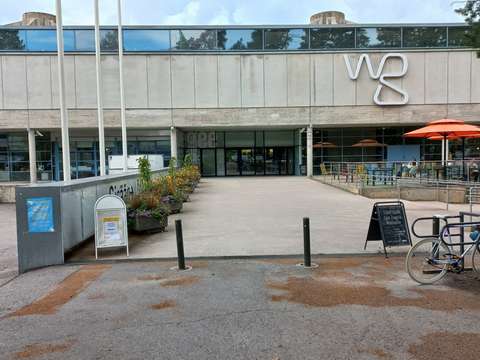 Betonisen näyttelykeskus WeeGeen lasiset ulko-ovet ovat jalkakäytävän perällä.