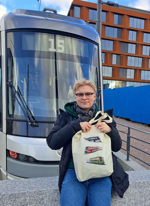Daniel Björklund sitter med en tygkasse i famnen på en mur framför snabbspårvagnen