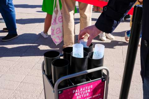 A hand drops a sparkling wine glass onto a rack of six black cones labelled as the dish collection point.