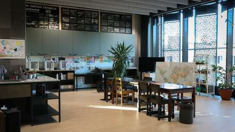 Avoin tila, jonka keskellä ja seinustoilla on pöytiä. Pöysillä on erilaisia pajalaitteita ja askartelutarvikkeita.