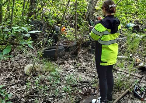 Huomioliiviin pukeutunut henkilö ottaa puhelimella kuvaa metsässä olevista roskista ja jätteistä.