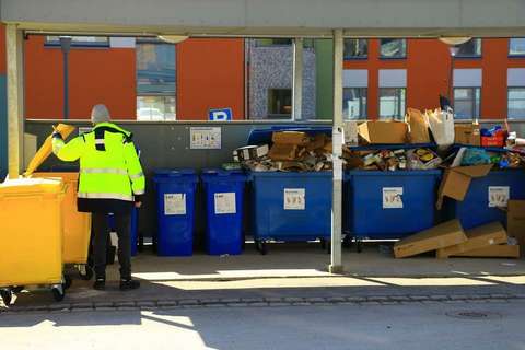 Huomioväriseen takkiin pukeutunut ihminen katsoo jäteastiaan. Vieressä täysiä jäteastioita.