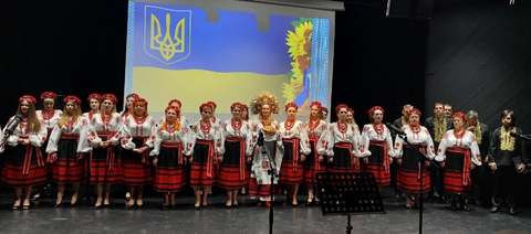 Kuoro lavalla kansallispukuihin pukeutuneina. Taustalla valkokankaalla kuva Ukrainan lipusta ja auringonkukista.