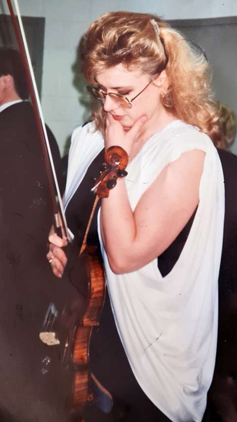 En kvinna med blont hår står med en fiol i handen.